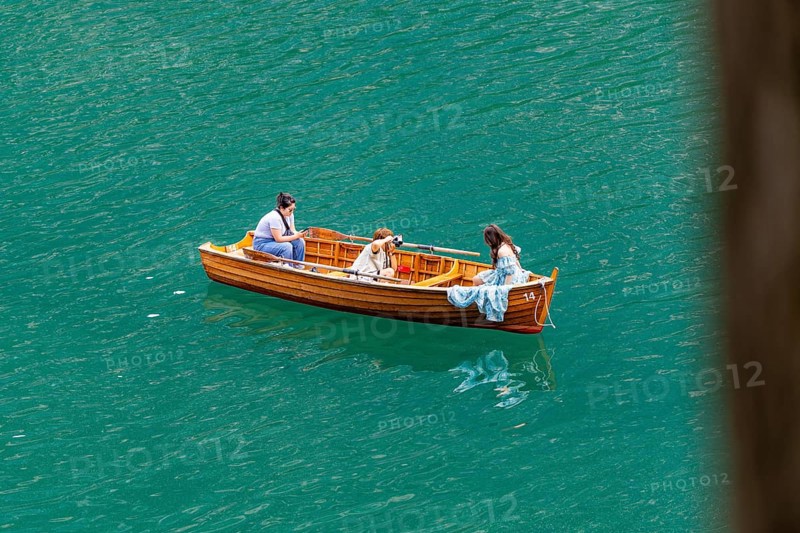 Three people in a wooden boat, floating relaxed on the water, in peaceful surroundings, Lake Braies, South Tyrol, Dolomites, Italy