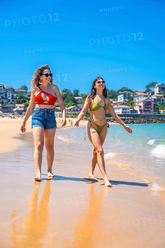 Two friends enjoying a sunny beach day, walking along the shore, laughing, and creating joyful memories together in the warm sand