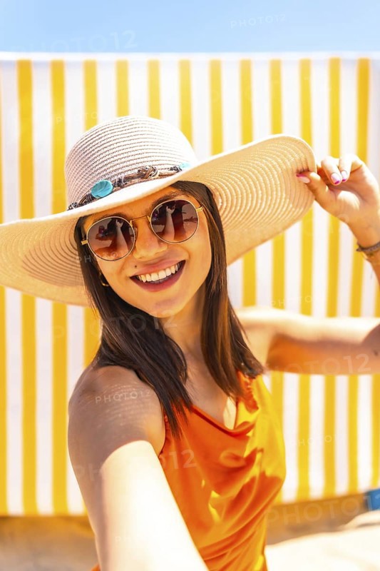 Fashionable tourist enjoying a sunny beach day, capturing joyful moments with a selfie while embracing the vibrant summer vacation vibe