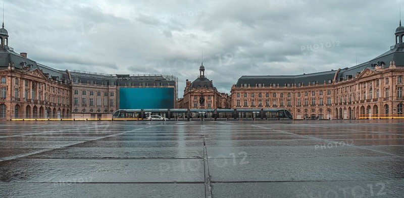 The stock exchange square in bordeaux, france, showcases its elegant architecture reflected on the wet pavement after a rainfall, with a modern tram passing through