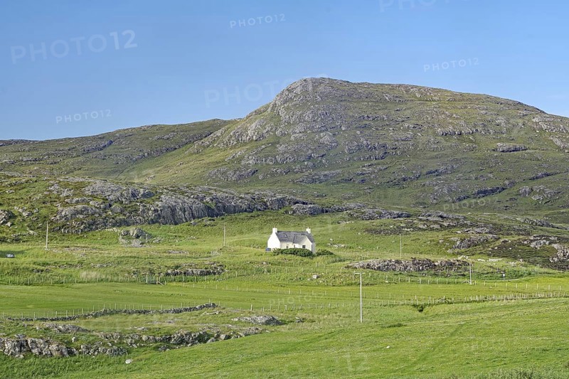 Small house in a green valley surrounded by mountains under clear skies, Isle of Barra, Hebrides, Scotland, United Kingdom