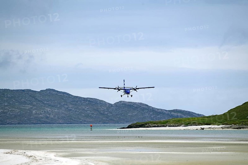 Small aeroplane approaching a beach surrounded by sea and mountains under a cloudy sky, Isle of Barra, Hebrides, Scotland, United Kingdom