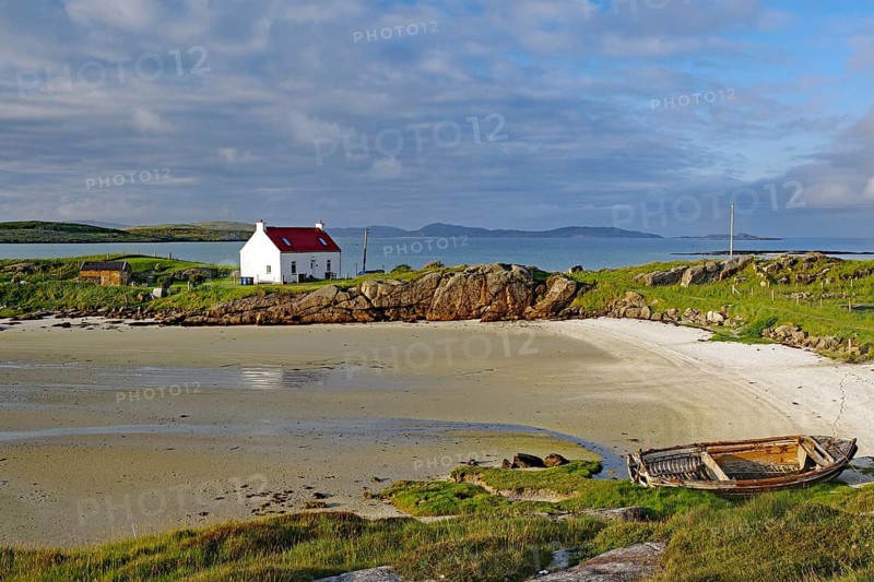 Boat wreck on a sandy beach with a white house and rocks in the background, Isle of Barra, Hebrides, Scotland, United Kingdom