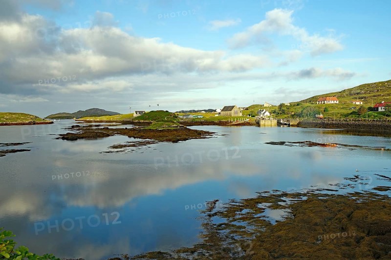 Calm lake in idyllic surroundings with clouds and houses in the background, evening mood, Isle of Barra, Hebrides, Scotland, Great Britain