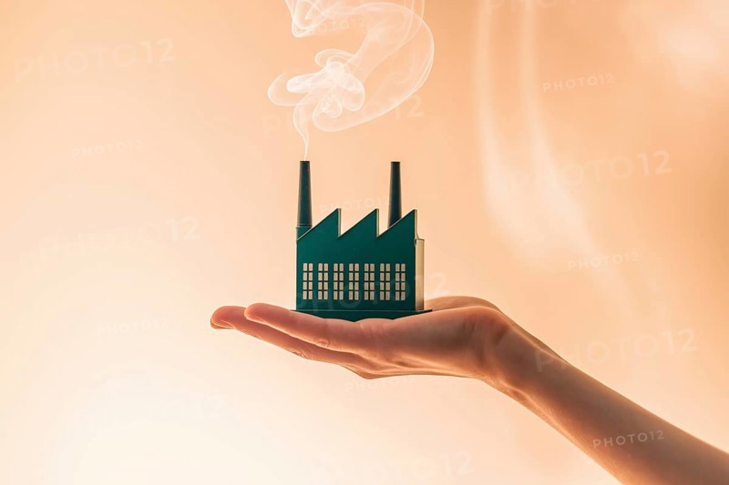 A detailed miniature green factory model with smoke held in hand against white background. Concept for greenwashing and environmental illusion. Generative ai, AI generated