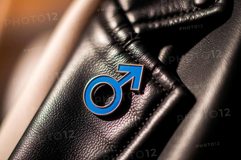 Close-up of blue male gender symbol pin on worn black leather jacket symbolizing masculinity and toxic patriarchy critique. Generative ai, AI generated