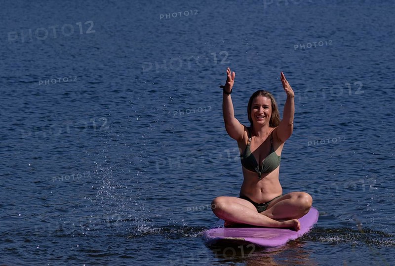 Woman, blonde, in bikini, sitting on board, surfboard, surfboard, purple, back, from behind, splashing with water. Bathing lake, lake, Schwaltenweiher near Seeg, Ostallgäu, Allgäu, Swabia, Bavaria, Germany