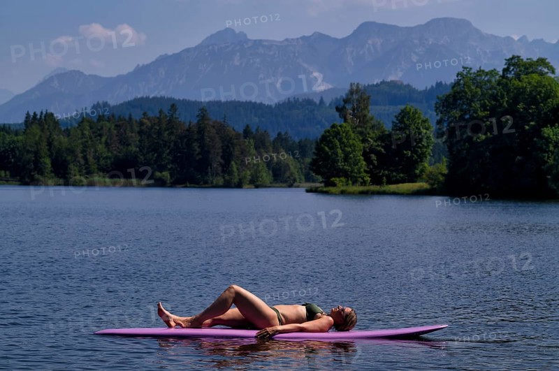 Woman, blonde, in bikini, lying on board, surfboard, surfboard, purple, relaxed, bathing lake, lake, Schwaltenweiher near Seeg, Allgäu Alps, East Allgäu, Allgäu, Swabia, Bavaria, Germany