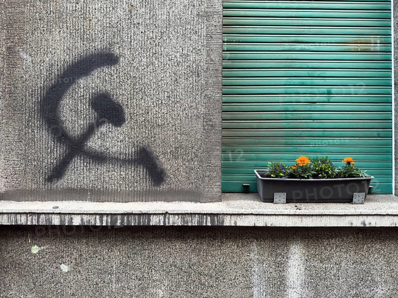 A hammer and sickle graffiti on a house wall next to a planted flower box in front of a roller shutter in Wuppertal, Germany