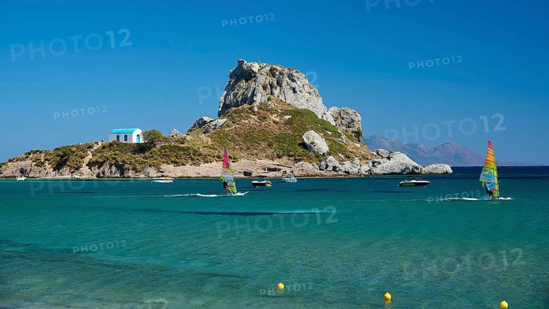 Island with windsurfers and boats in the turquoise blue sea in front of a rocky coast, Agios Stefanos Beach, Agios Stefanos Basilica, Chapel of Agios Nikolaos, Kastri Island, Kos, Dodecanese, Greek Islands, Greece
