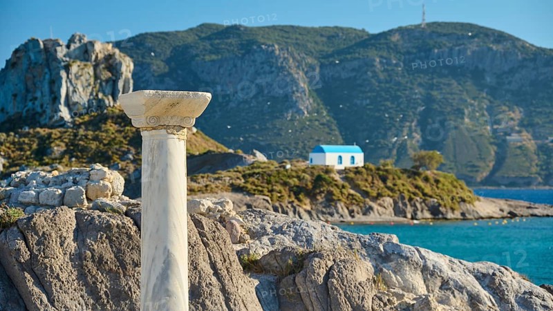Stone column in front of island with chapel and blue roof, surrounded by azure blue sea, Agios Stefanos Beach, Agios Stefanos Basilica, Chapel Agios Nikolaos, Kastri Island, Kos, Dodecanese, Greek Islands, Greece