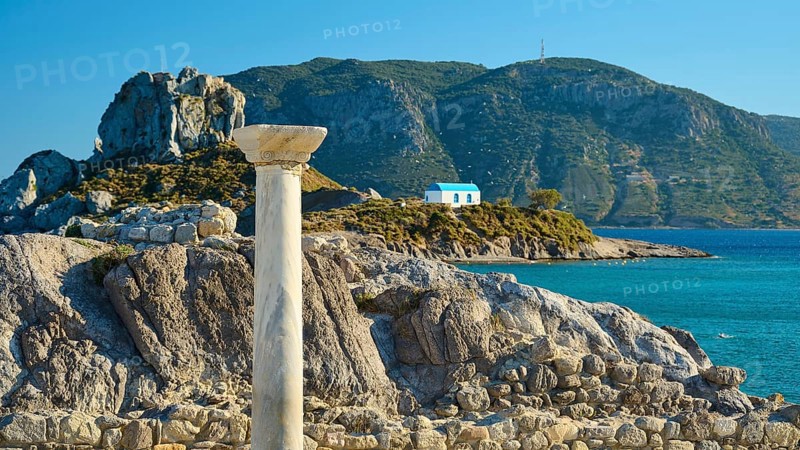 Ancient column and stones in front of island with chapel, blue sky in the background, Agios Stefanos Beach, Agios Stefanos Basilica, Chapel Agios Nikolaos, Kastri Island, Kos, Dodecanese, Greek Islands, Greece