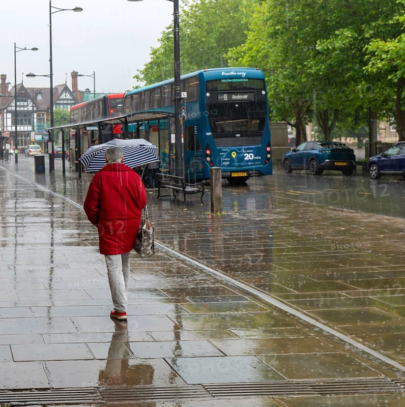 Woman with umbrella walking in heavy rain, city centre of Salisbury, Wiltshire, England, UK