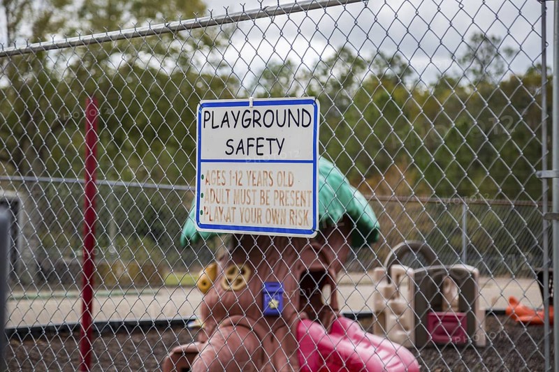 Sign with playground safety rules on a chain link fence surrounding a childrens palyground