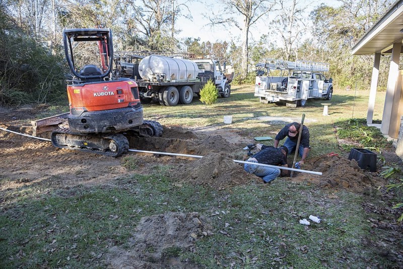 Workers installing pipe connecting new water well to house plumbing in rural area of Gulfport, Mississippi, USA