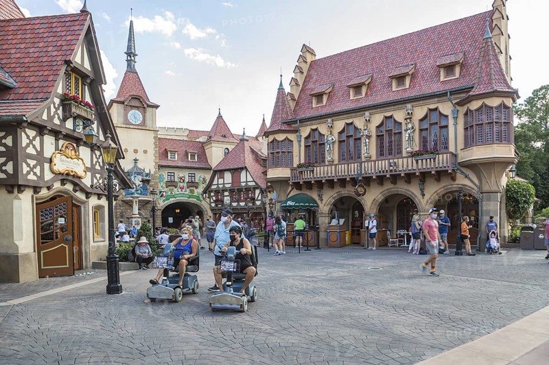 Masked park guests walking and riding scooters through the Germany pavilion of Epcot at Walt Disney World in Orlando, Florida
