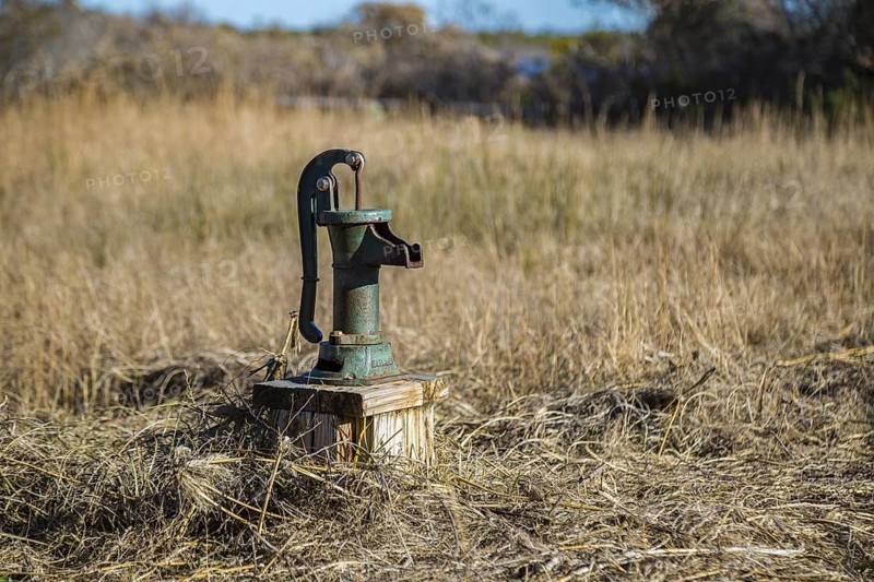 Old fashioned manual hand pump on water well in grassy field