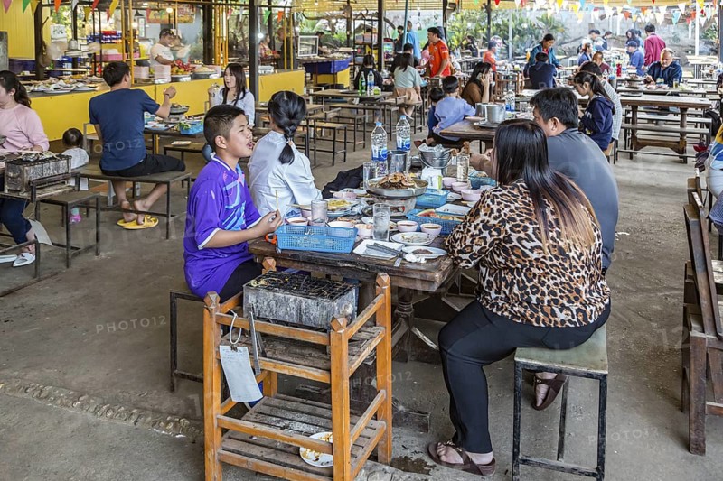 Thai family cooking food on charcoal grill and hot pot at their table in a buffet style outdoor restaurant in Chiang Rai province of Northern Thailand
