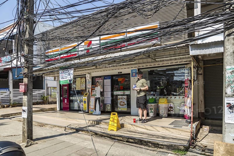 American tourist standingunder a tangled mess of utility wires outside a 7 Eleven store in Chiang Rai province of Northern Thailand