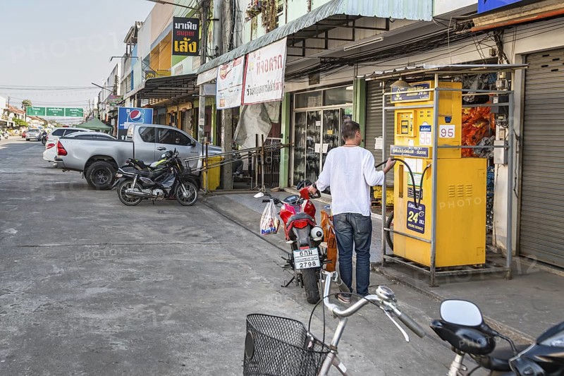 Thai man filling motor scooter with gasoline from a remote Sun Oil pump in Chiang Rai, Thailand
