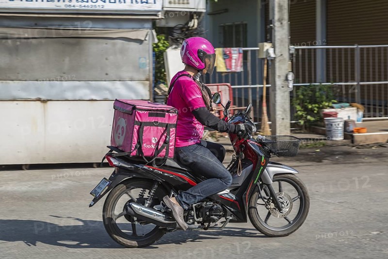 Food delivery drivers and other Thai motor scooter riders at a traffic light in Chiang Rai, Thailand