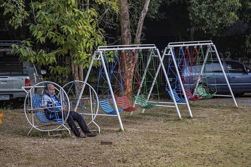 Thai man sitting alone on a childs playground swing in Chiang Rai, Thailand