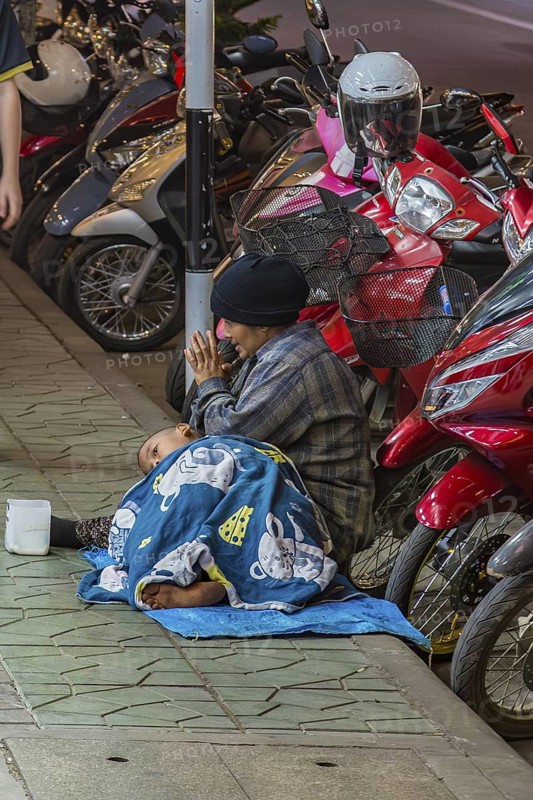 Homeless woman and son begging for money on the downtown street at night in Chiang Rai, Thailand