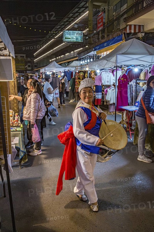 Smiling Thai woman beating a drum as she dances through the Night Market in downtown Chiang Rai, Thailand