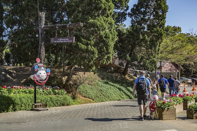 American tourists walking past a sign pointing to the entrance to the Doi Tung Royal Villa inside the Doi Tung tourist attraction in Chiang Rai, Thailand