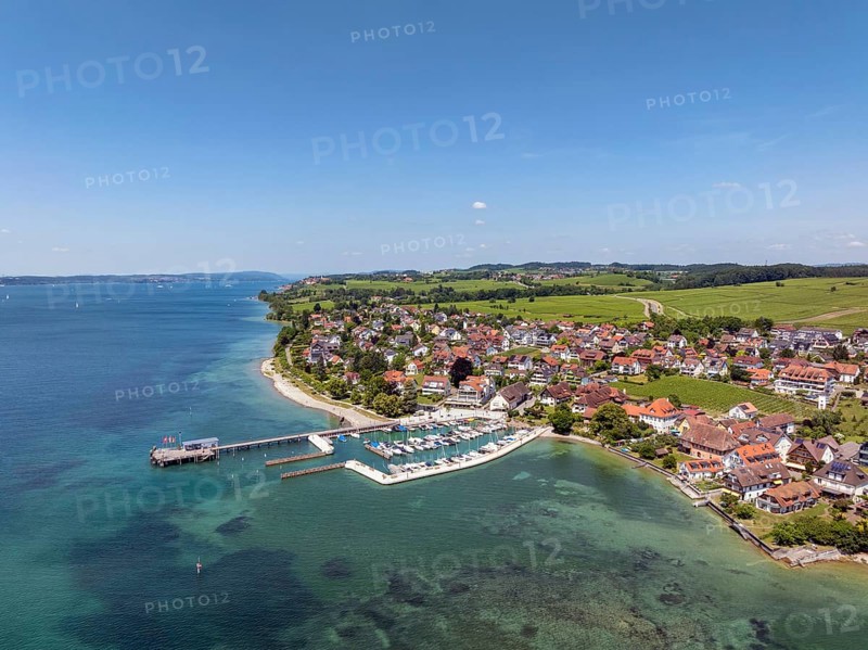 Luftbild von der Bodenseegemeinde Hagnau, Winzerdorf und beliebter Ferienort am Bodensee, dahinter Rebhänge, auf denen hauptsächlich die Weinsorten Müller Thurgau und Blauer Burgunder angebaut werden. Am Seeufer der am 23.Mai 2025 eingeweihte, neue Westhafen, Yachthafen mit der Schiffanlegestelle, Bodenseekreis, Baden-Württemberg, Deutschland