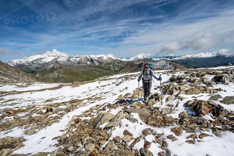 Mountaineer in blocky terrain with fresh snow in summer, ascent to the summit Böses Weibl, view of mountain landscape with snow-covered summit of the Großglockner, Wiener Höhenweg, Schober group, Hohe Tauern National Park, Carinthia, Austria