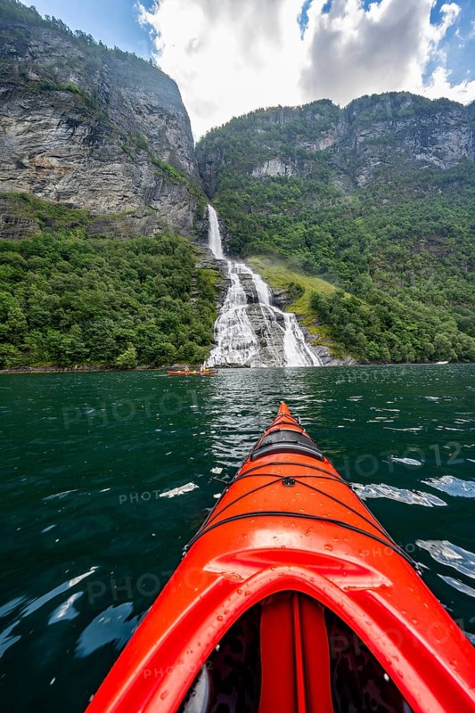 Kayak trip on the Geirangerfjord at the Freier waterfall, tip of a red kayak in the fjord, atmospheric fjord landscape, first person view, near Geiranger, Møre og Romsdal, Norway