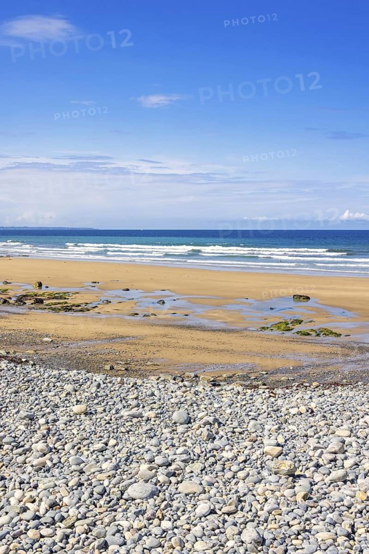 Pebble beach by the sea with a seascape view to the horizon and breaking waves on the shore a sunny summer day with a blue sky, Crozon peninsula, Bretagne, France
