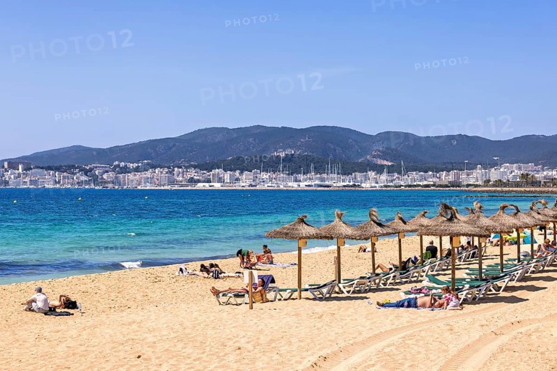 Sand beach by the blue mediterranean sea with sunbathing people at sun lounger and the palma city in the background a sunny day by the sea, Palma de Mallorca, Mallorca, Spain