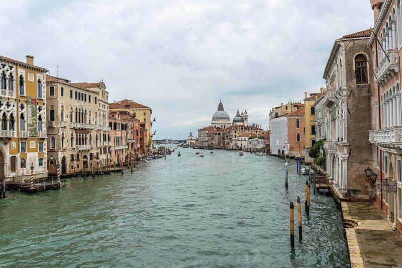 Scenic view of the grand canal flowing through venice, showcasing colorful historic buildings and the majestic basilica di santa maria della salute under a cloudy sky