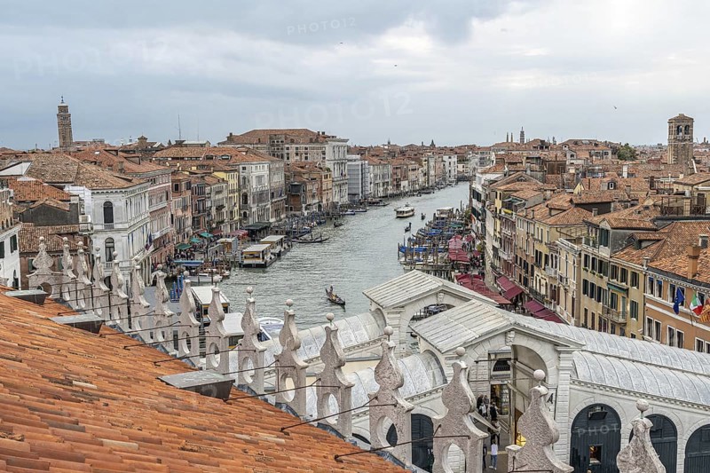 Gondolas navigating the grand canal amidst historic buildings in venice, italy, seen from a rooftop with terracotta tiles
