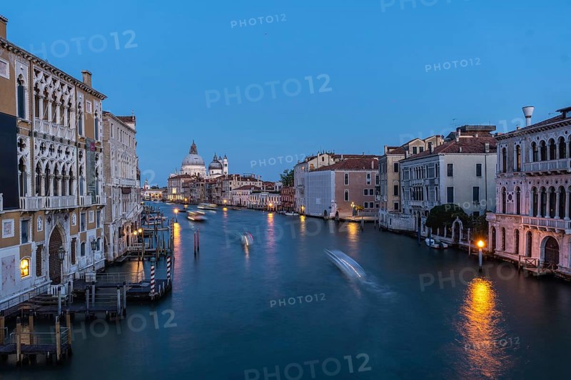 Motorboats creating motion blur are navigating grand canal with basilica di santa maria della salute in background at blue hour