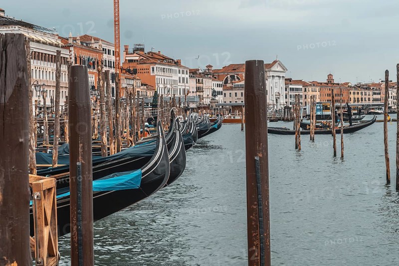 Gondolas moored near the rialto bridge in venice, waiting patiently for tourists on a cloudy day, create a serene and picturesque scene