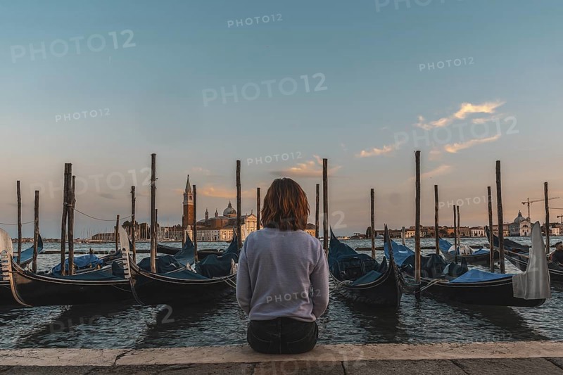 Young woman enjoying the sunset over the venetian lagoon with gondolas moored in the foreground and the san giorgio maggiore church in the background