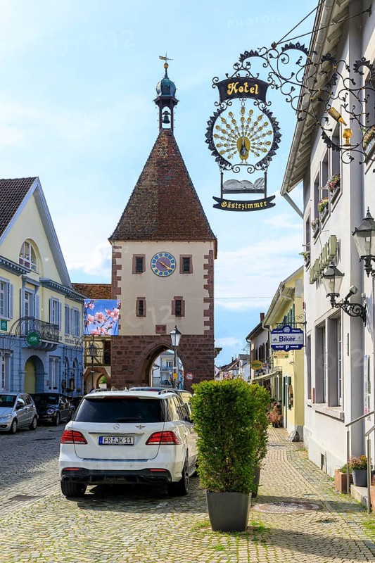 Special sign of the Hotel Pfauen, in the background the Königschaffhausen Tor, an old town gate of Endingen am Kaiserstuhl, Baden-Württemberg, Germany