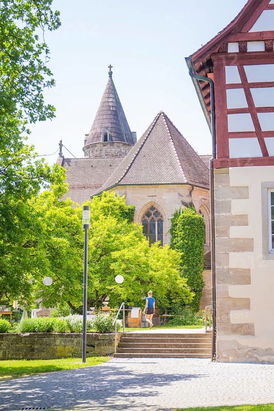 Church tower towers over green trees next to a half-timbered building in summer weather, event and wedding location Lorch Monastery, Lorch, Germany