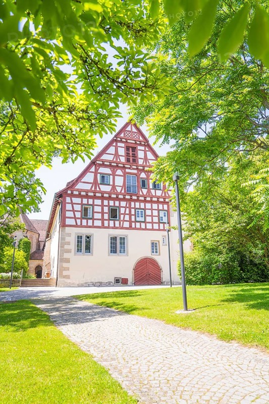 Half-timbered house with cobblestone path and surrounded by green trees under a clear sky, event and wedding location Lorch Monastery, Lorch, Germany