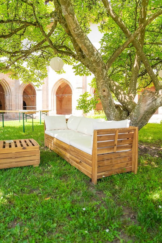 Wooden sofa under a tree in the garden with cushions, located in a shady forecourt, event and wedding location Kloster Lorch, Lorch, Germany