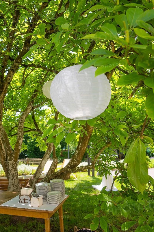 Paper lantern hanging from a tree above a table with crockery in the summer garden, event and wedding location Kloster Lorch, Lorch, Germany
