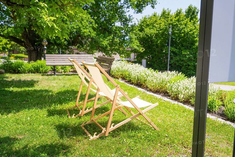 Two wooden deckchairs in the summer garden on a green lawn next to trees in the shade, event and wedding location Lorch Monastery, Lorch, Germany