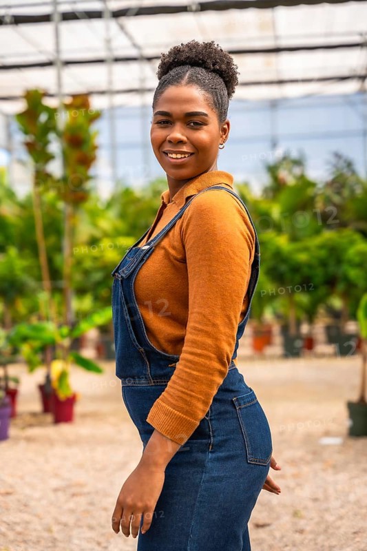 Confident young black woman tending to vibrant plants and flowers in a greenhouse, nurturing growth and showcasing her passion for gardening