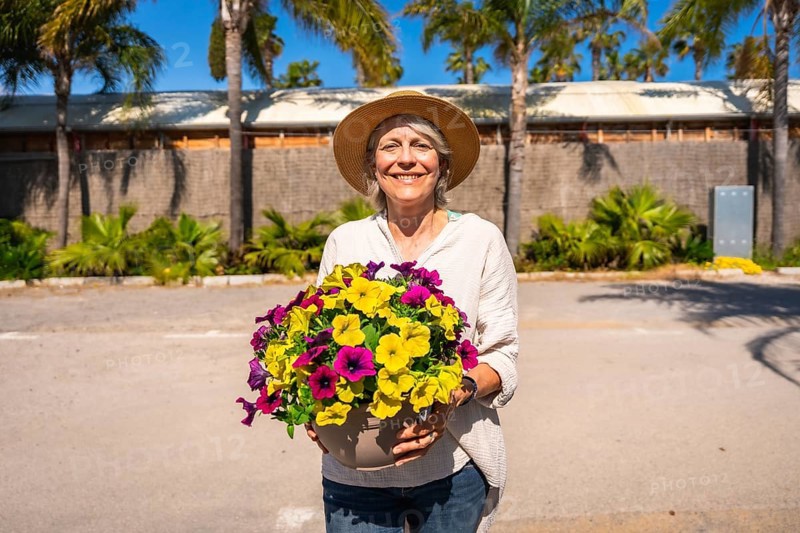 Happy gardener holding a pot of colorful petunias, enjoying a sunny day at the botanical garden