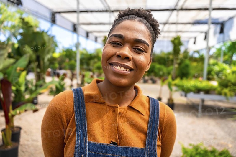 Portrait of a young african american woman working in a greenhouse, smiling confidently amidst lush greenery