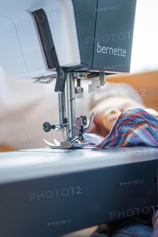 Close-up of the needle of a sewing machine sewing a chequered fabric in a well-lit room