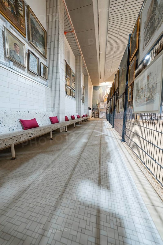 A long corridor in an art gallery with numerous paintings on the walls and a white bench with red cushions, historical art exhibition in the old swimming pool, Schaudepot, Calw, Black Forest, Germany